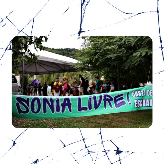 Faixa verde com os dizeres “Sônia Livre! Basta de escravidão” estendida em frente a um ato público ao ar livre, com pessoas reunidas sob tendas e árvores ao fundo