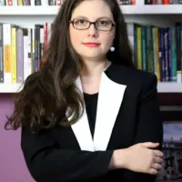 Vivian é uma mulher branca de cabelos longos, que usa óculos, brincos no formato de pérola e veste blazer preto e branco