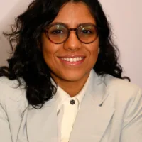 Mulher negra de pele clara com cabelos ondulados longos, que usa óculos e está sorrindo