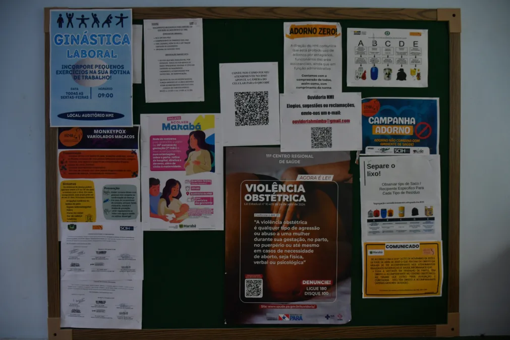 O quadro de avisos mostra cartazes informativos sobre temas diversos, incluindo violência obstétrica, descarte de lixo, campanhas de saúde e ginástica laboral.