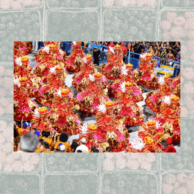 A imagem mostra a ala das baianas elaboradas em vermelho e dourado, adornadas com plumas brancas em um desfile de carnaval. Elas ocupam toda a avenida, cercadas por arquibancadas lotadas de espectadores. A fotografia está em uma moldura preenchida por padrões de frutas estilizadas.