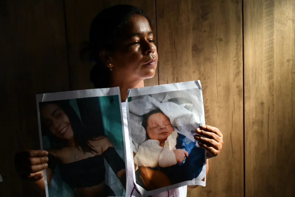 A imagem mostra uma mulher com expressão séria segurando duas fotos: uma de uma jovem sorridente e outra de um bebê enrolado em um cobertor.