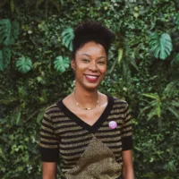 Graziela é uma mulher negra de cabelo crespo curto, usando uma blusa preta, uma gargantilha e sorrindo
