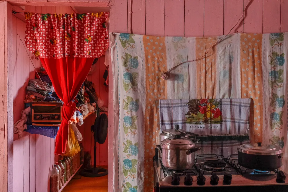 casa de madeira rosa com cortina vermelha, fogao com panelas, roupas expostas, nao ha guarda-roupas nem porta na casa