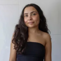 Amanda é uma mulher parda de cabelos castanhos longos, ela usa uma blusa tomara-que-caia preta e tem uma expressão leve