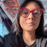 Catarina é uma mulher parda, de cabelos lisos na altura dos ombros, que usa óculos de armação vermelha e blusa preta