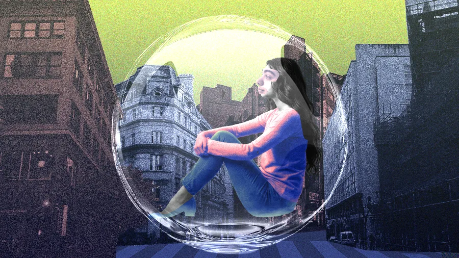 A imagem mostra uma colagem de uma mulher sentada com os joelhos abraçados dentro de uma bolha transparente gigante. A bolha está posicionada no meio de uma rua de cidade com prédios altos ao fundo, sugerindo isolamento.