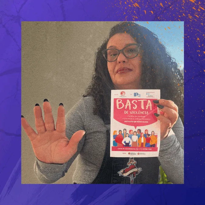 Silvana é uma mulher de cabelos cacheados e óculos levanta uma das mãos em sinal de “pare” e segura um panfleto com a frase “Basta de violência” em destaque. Ela veste blusa cinza e jardineira preta com estampa na frente.