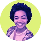 Mulher negra de cabelos crespos e curtos. Ela está sorrindo e usando uma blusa branca com sobreposição estampada.