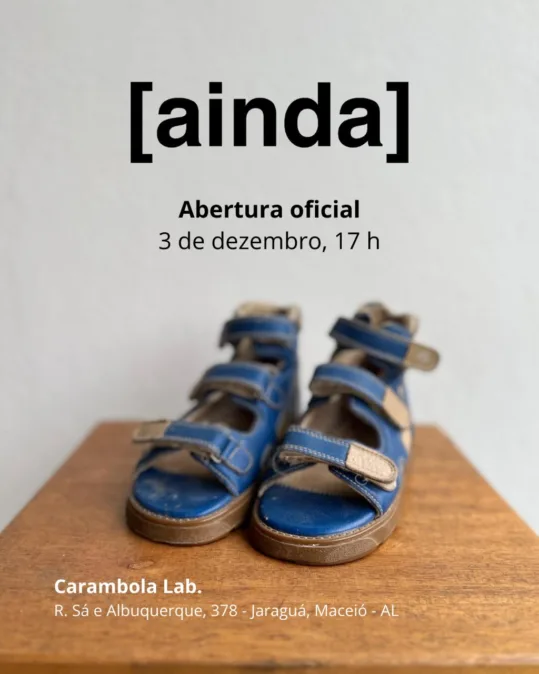 Cartaz com fundo claro. No topo, título em preto: [ainda]. Abaixo, em negrito: Abertura oficial e, na linha seguinte, 3 de dezembro, 17 h. Na metade inferior, foto de um par de sandálias infantis ortopédicas azul-marinho, com velcros bege, apoiadas sobre uma superfície de madeira; foco nas sandálias e fundo desfocado. No rodapé, em branco: Carambola Lab. e o endereço R. Sá e Albuquerque, 378 – Jaraguá, Maceió – AL.