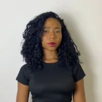 Mulher negra de cabelos pretos longos e cacheados, usando uma blusa preta