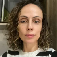 Mulher branca de cabelos cacheados castanhos na altura dos ombros, usando uma blusa preta e branca