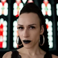 Mulher branca, de cabelos presos, usando batom preto e brincos grandes