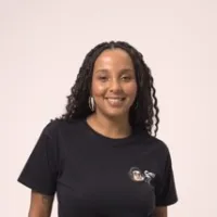 Mulher negra não retinta de cabelo preto longo e trançado. Ela sorri e usa uma blusa preta.