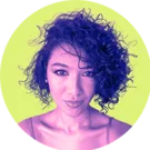 Flávia Santos está de frente, com expressão serena, olhando para a câmera. Tem cabelo curto escuro, cacheado, repartido de lado. A imagem usa um filtro em tons roxos e rosas sobre a pele e o cabelo, contrastando com um fundo verde-limão. Ela veste uma blusa de alça fina.