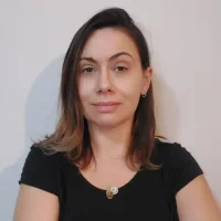 Priscila é branca, tem cabelos castanhos claros e lisos um pouco abaixo dos ombros, e está usando uma blusa preta