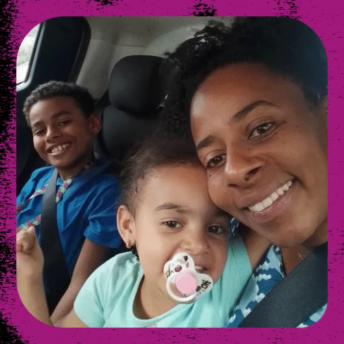 Jéssica é uma mulher negra, de cabelos curtos. Na foto ela está dentro de um carro com os dois filhos autistas