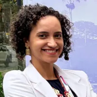 Natalia é uma mulher negra de pele clara, com cabelos cacheados curtos e castanho escuro