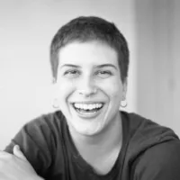 Ju é um homem trans de pele branca e cabelos curtos. Usa uma argola e está sorrindo