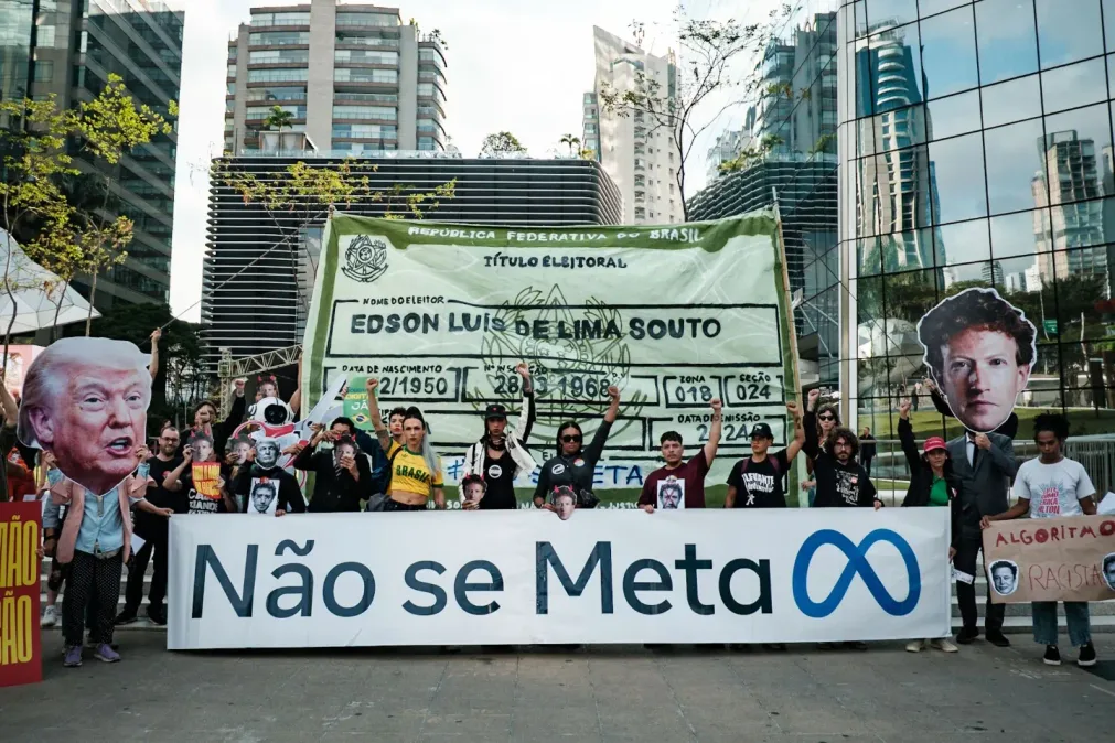 Manifestantes protestam contra a Meta e o poder dos algoritmos nas eleições, com cartazes que criticam Mark Zuckerberg, Donald Trump e a atuação das redes sociais.