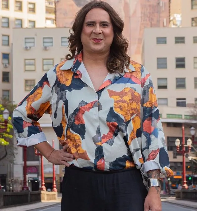 Duda Salabert posa em uma rua, com camisa estampada em tons de laranja, azul, branco e preto.